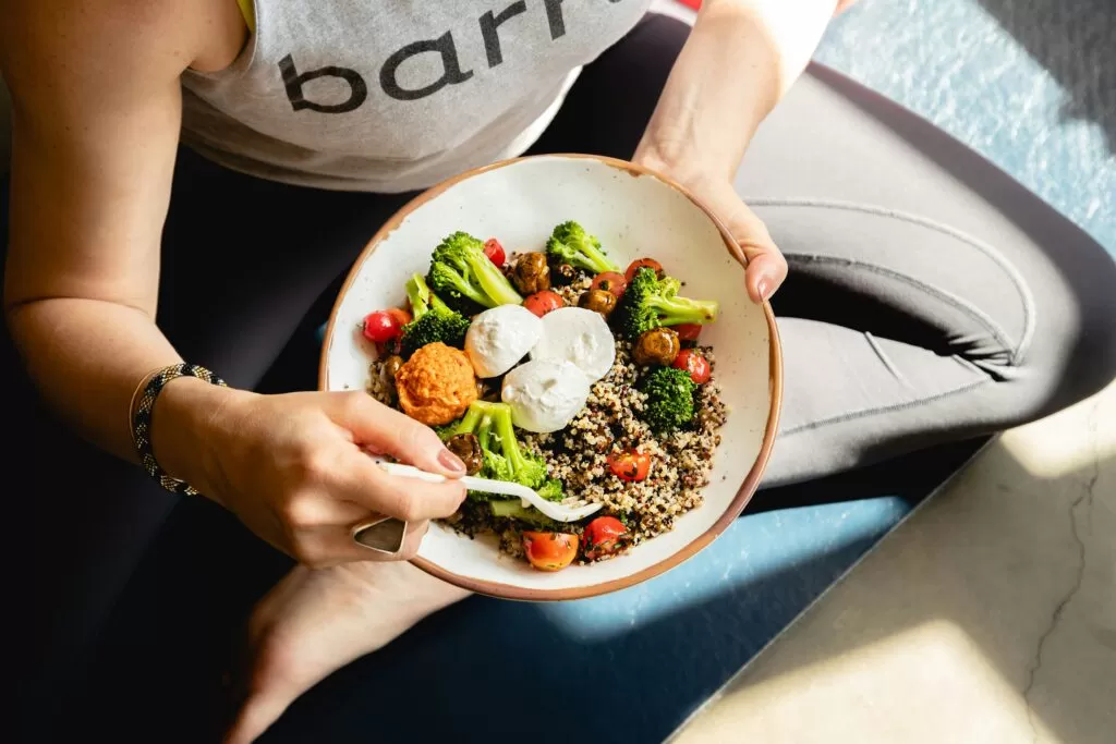 Mulher sentada de perna de índio no chãosegurando uma tijela com legumes e grãos
